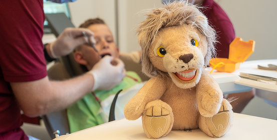 Kinderzahnheilkunde: Zahnputz-Löwe und Kind bei Zahnbehandlung